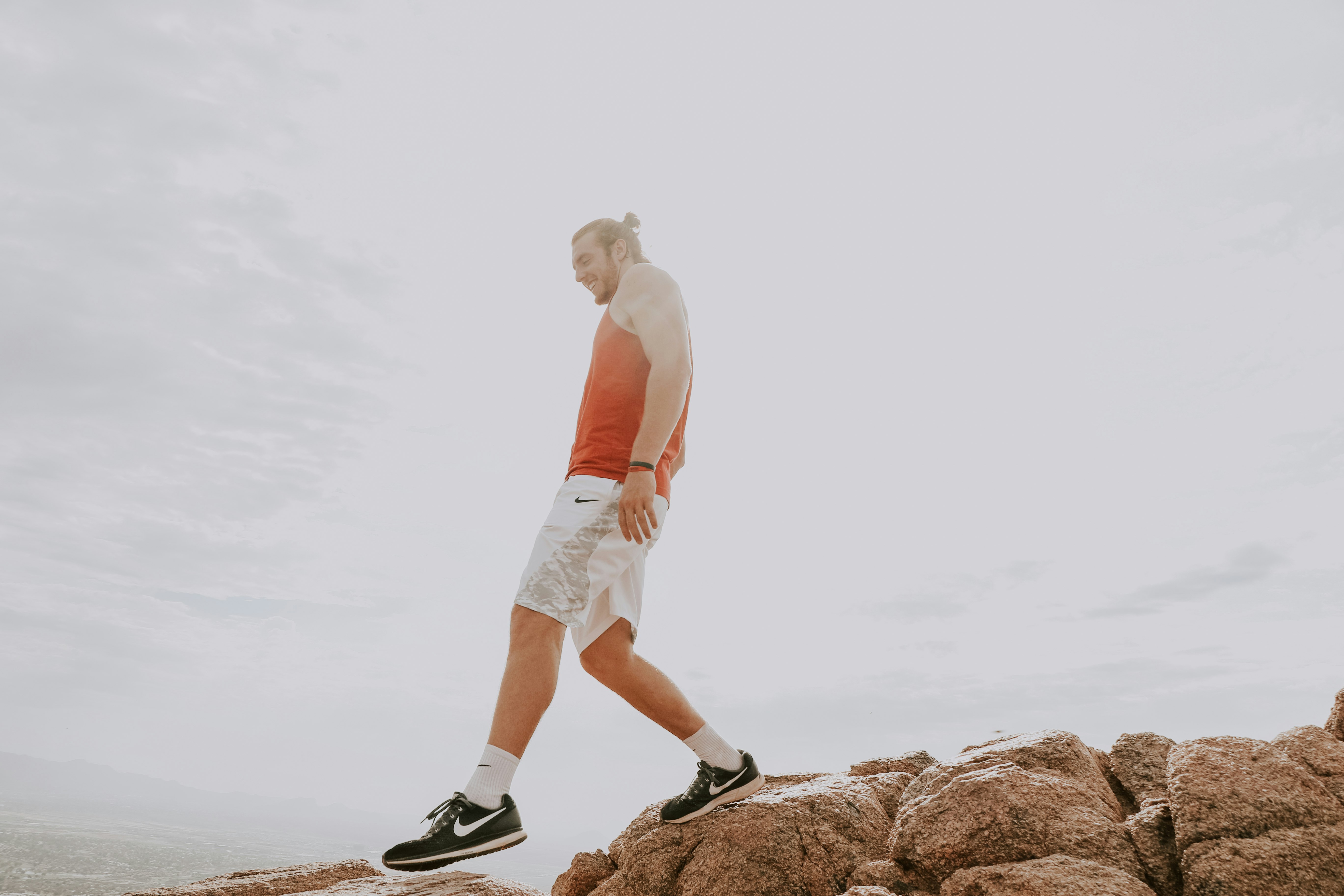 man wearing orange tank top standing on brown rocks